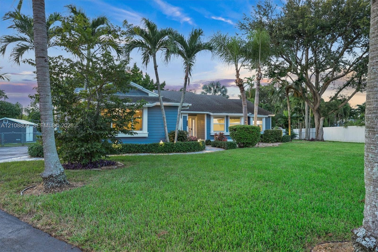 Single-story residence featuring lap siding, mature palm trees, manicured lawn, and perimeter fencing
