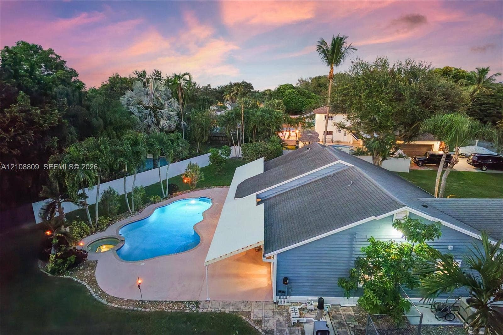 Backyard featuring an in-ground swimming pool with an integrated spa, a concrete pool deck, a covered patio, and mature landscaping