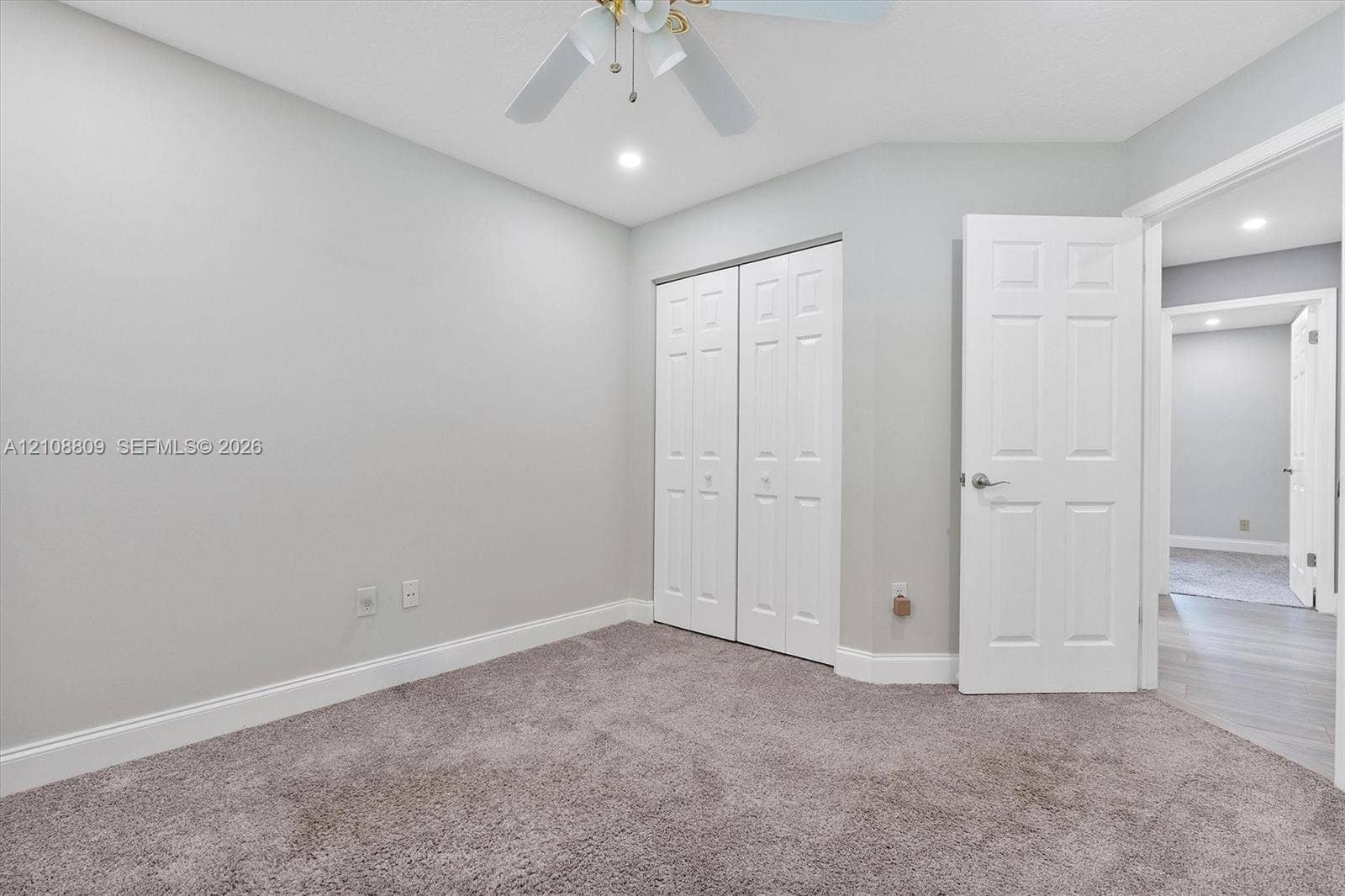Neutral wall tones, carpeted flooring, bi-fold closet doors, six-panel interior door, and a ceiling-mounted light fixture with a fan