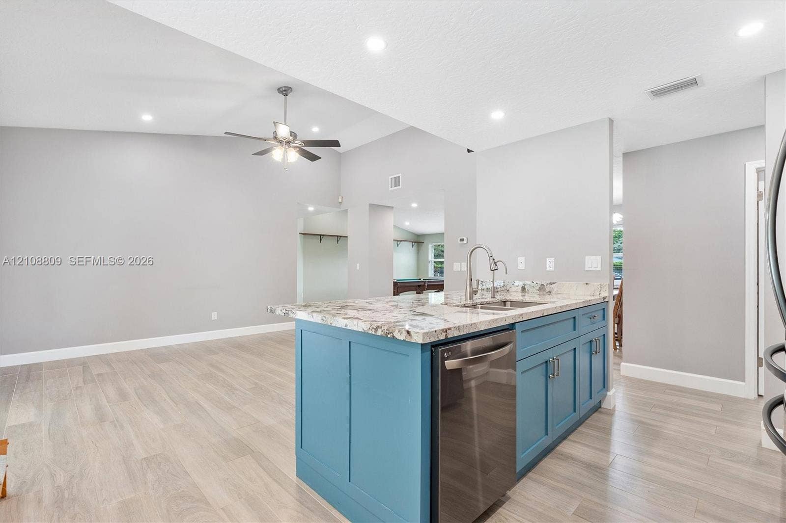 Kitchen island with stone-finish countertop, undermount sink, blue shaker-style cabinetry, stainless steel dishwasher, and wood-finish flooring