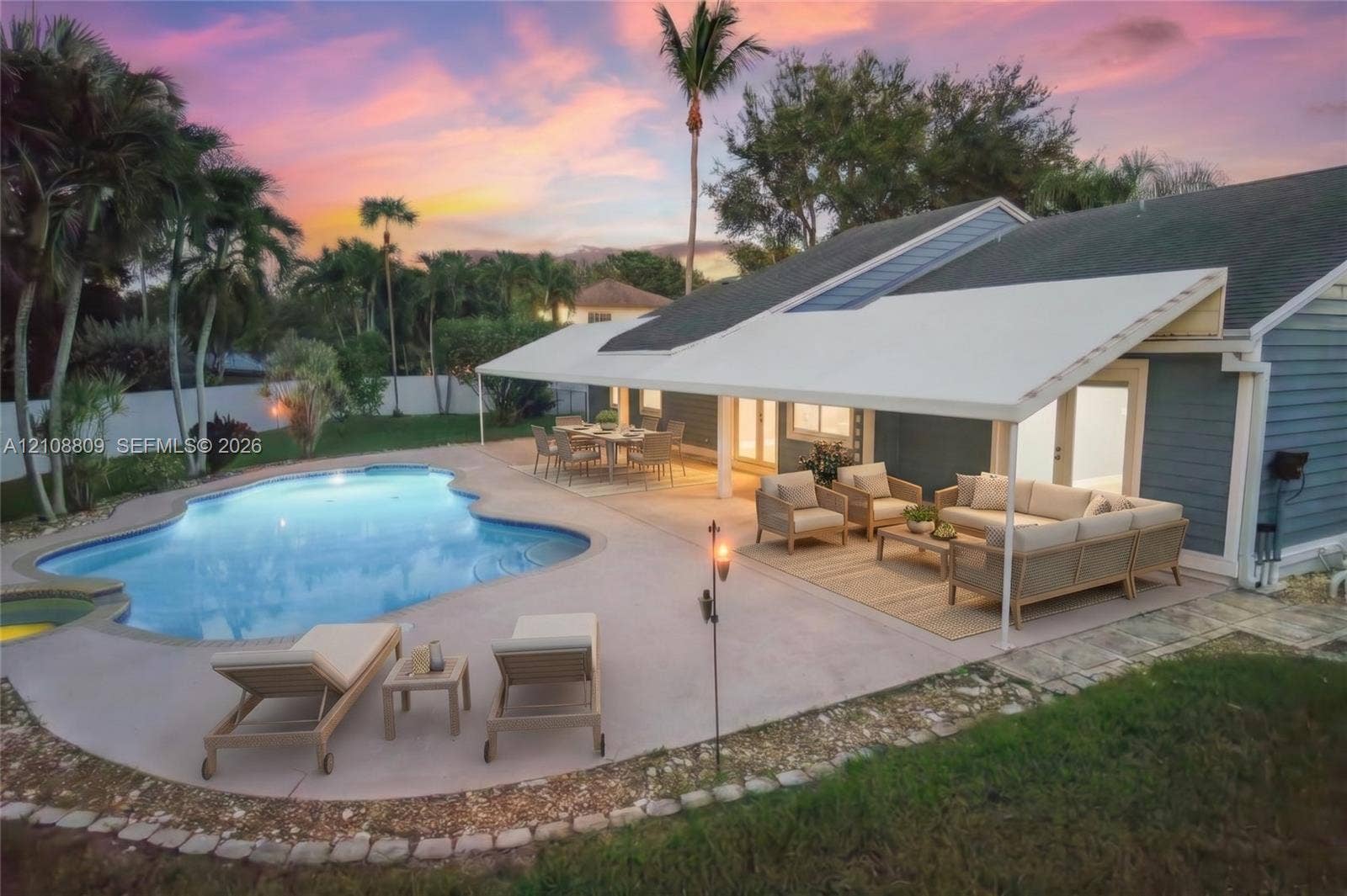 Custom-shaped inground swimming pool with a sprawling concrete patio, expansive covered lanai, and solid-color siding exterior