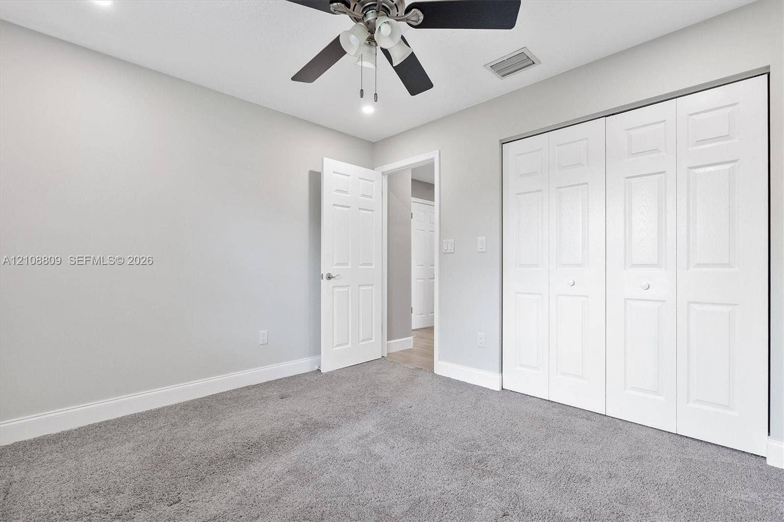 Interior room featuring neutral-tone carpeting, a multi-panel door, a multi-panel closet door, and a ceiling fan with integrated lighting