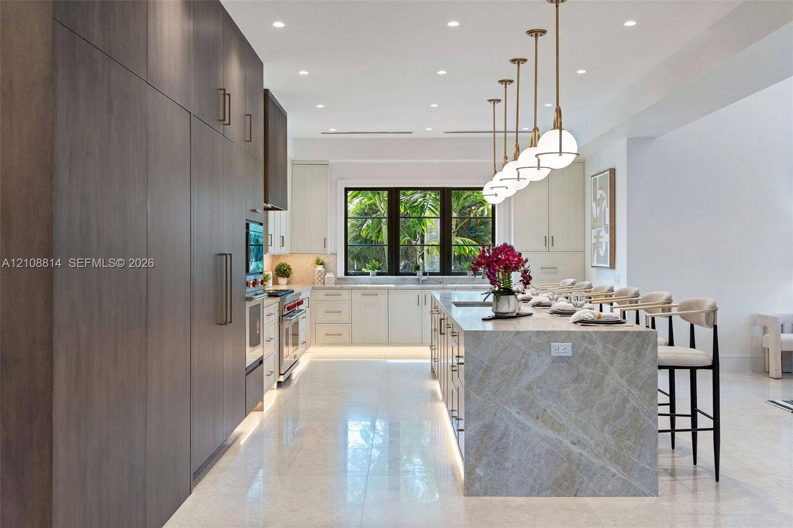 Kitchen featuring floor-to-ceiling cabinetry, a waterfall-edge stone island, recessed ceiling lighting, a row of spherical pendant lights, and large-format tile flooring
