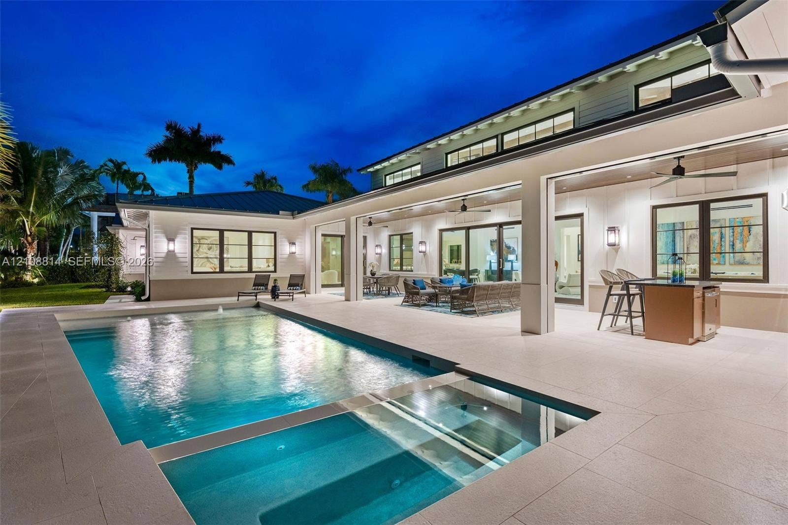 Covered outdoor patio with stone tile flooring, built-in outdoor kitchen, swimming pool with integrated spa, and expansive multi-panel sliding glass doors