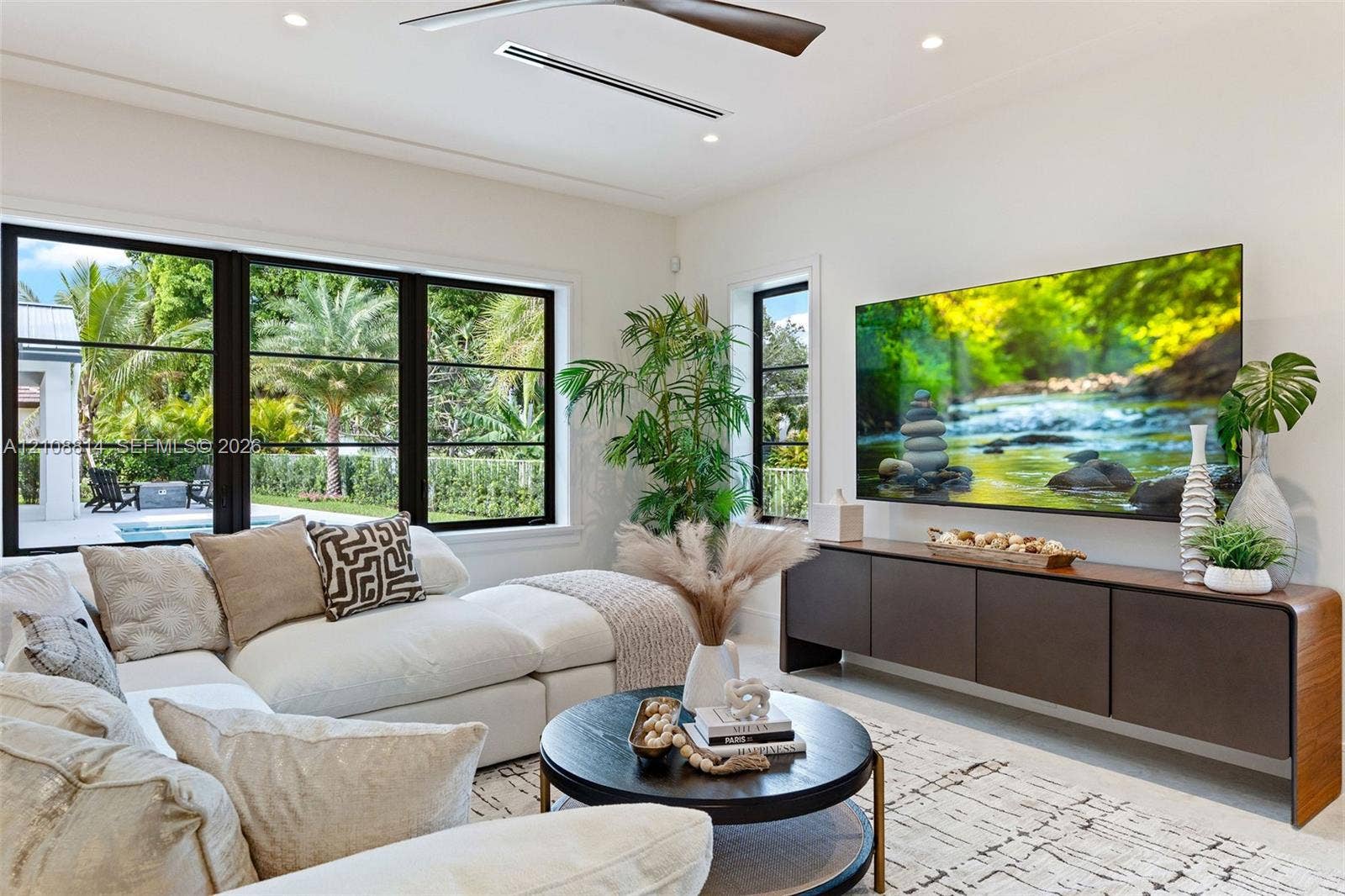 Living space featuring black-framed picture windows, recessed lighting, ceiling fan with wood-finish blades, and custom built-in cabinetry with a curved profile