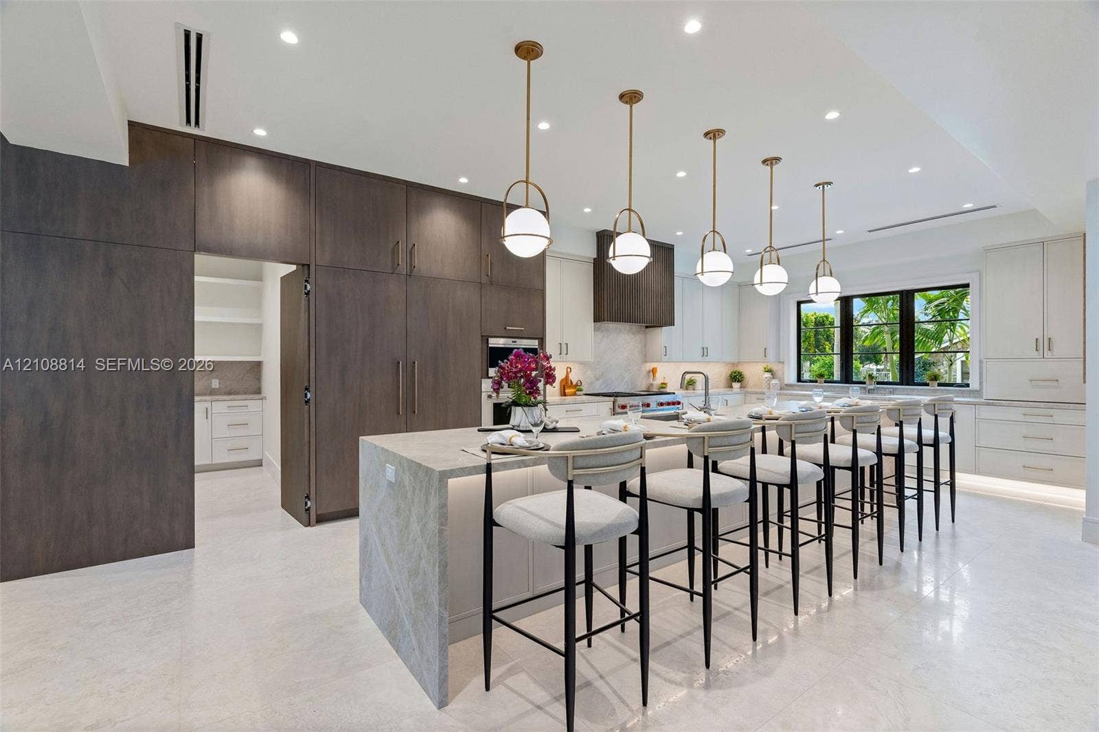Kitchen featuring a waterfall-edge center island, two-tone custom cabinetry, stone-style countertops, professional-grade stainless steel appliances, and tiered globe pendant lighting