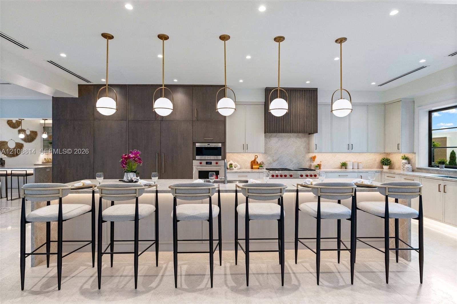 Kitchen featuring a large central island with waterfall-edge stone countertop, custom cabinetry, integrated professional-grade appliances, recessed lighting, and a series of globe-style pendant lights
