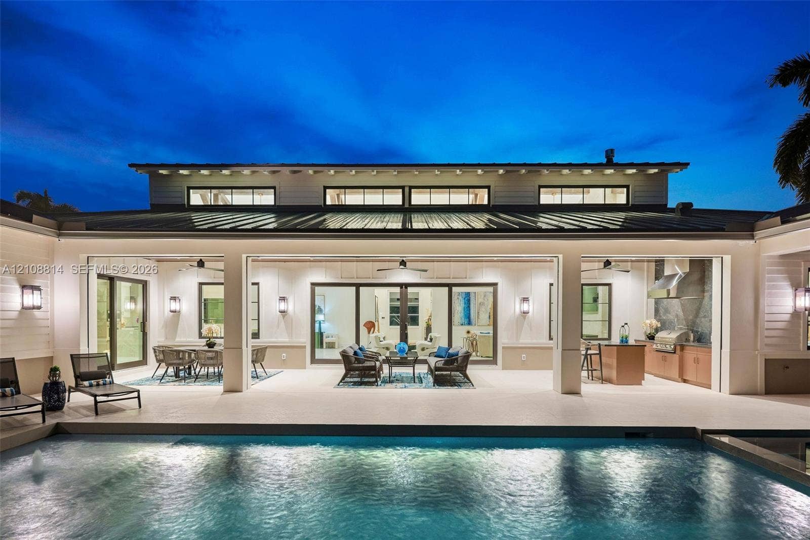 Covered outdoor living area featuring a metal roof, expansive glass door openings, built-in outdoor kitchen with cabinetry, integrated ceiling fans, and a private swimming pool
