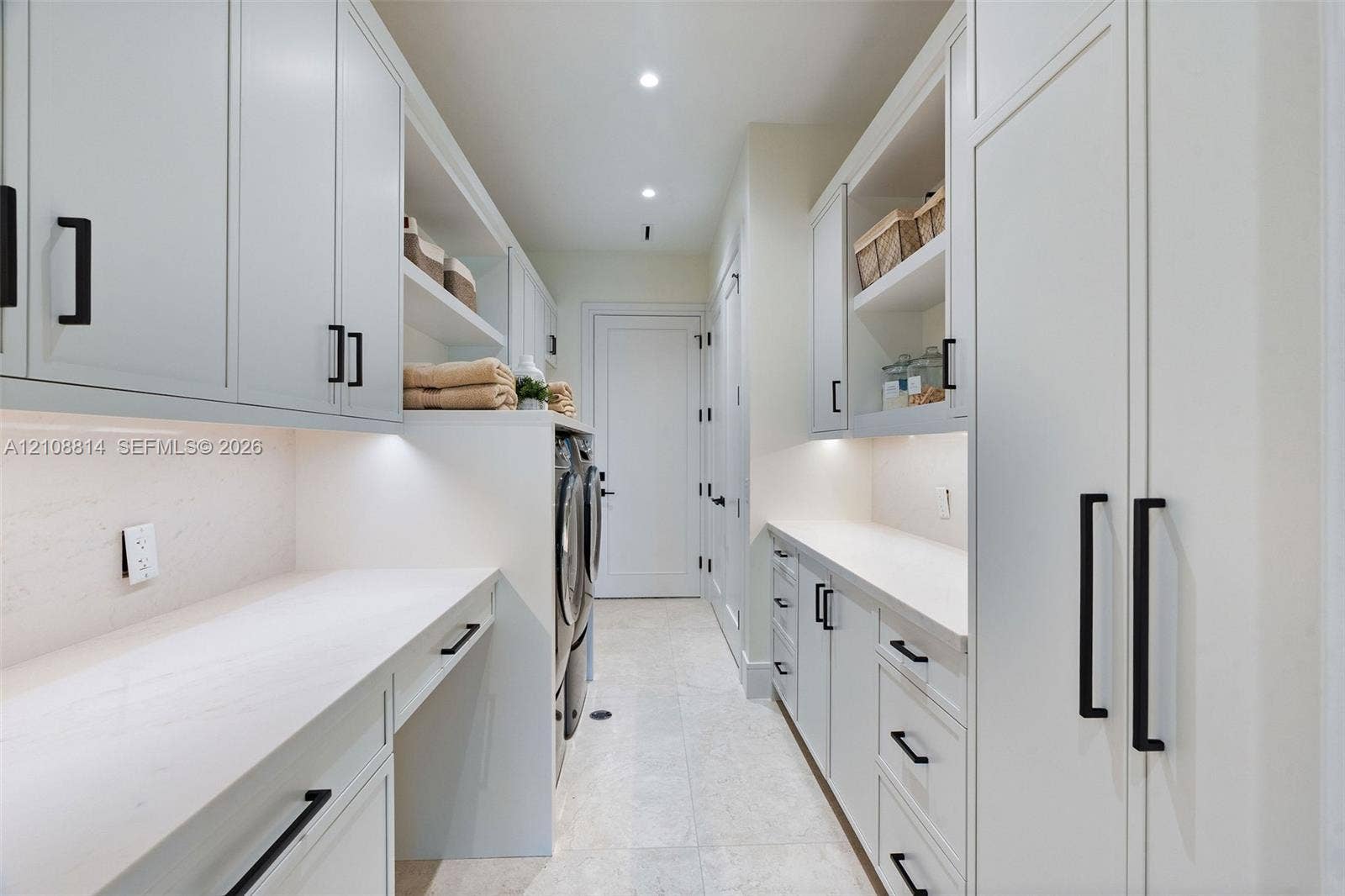 Custom cabinetry with matte black hardware, stone countertops, integrated under-cabinet lighting, and light-toned tile flooring