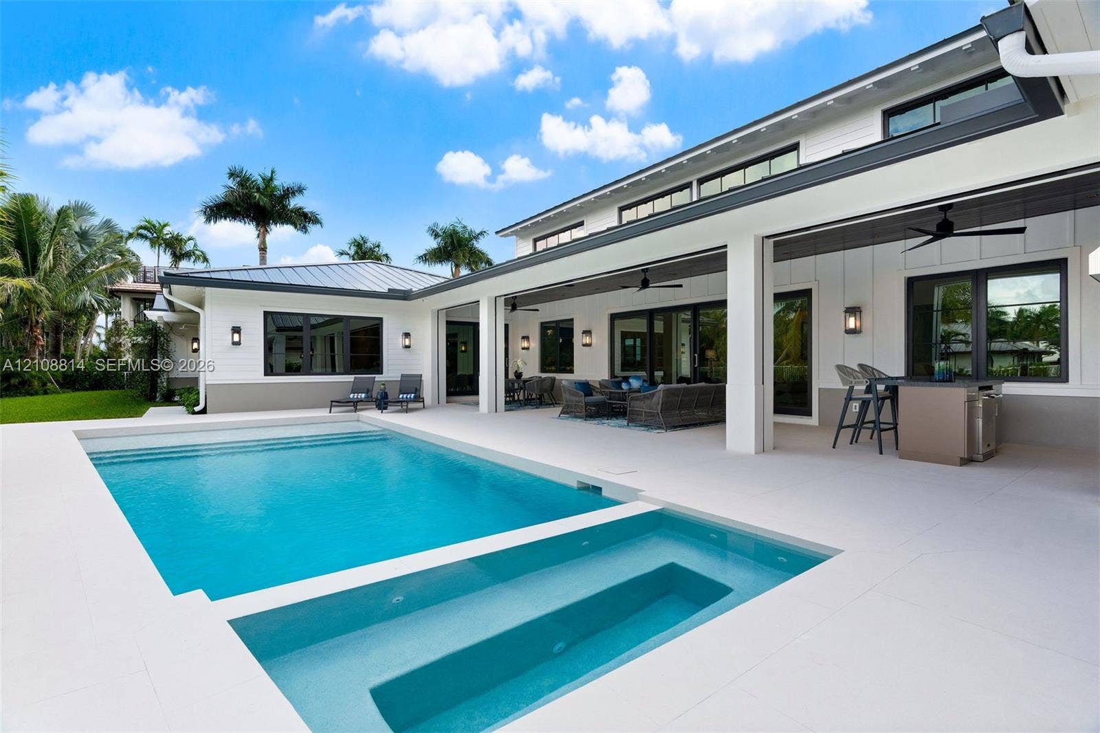 Modern exterior featuring board-and-batten siding, a covered patio with integrated ceiling fans, a built-in outdoor kitchen, and a swimming pool with a built-in spa