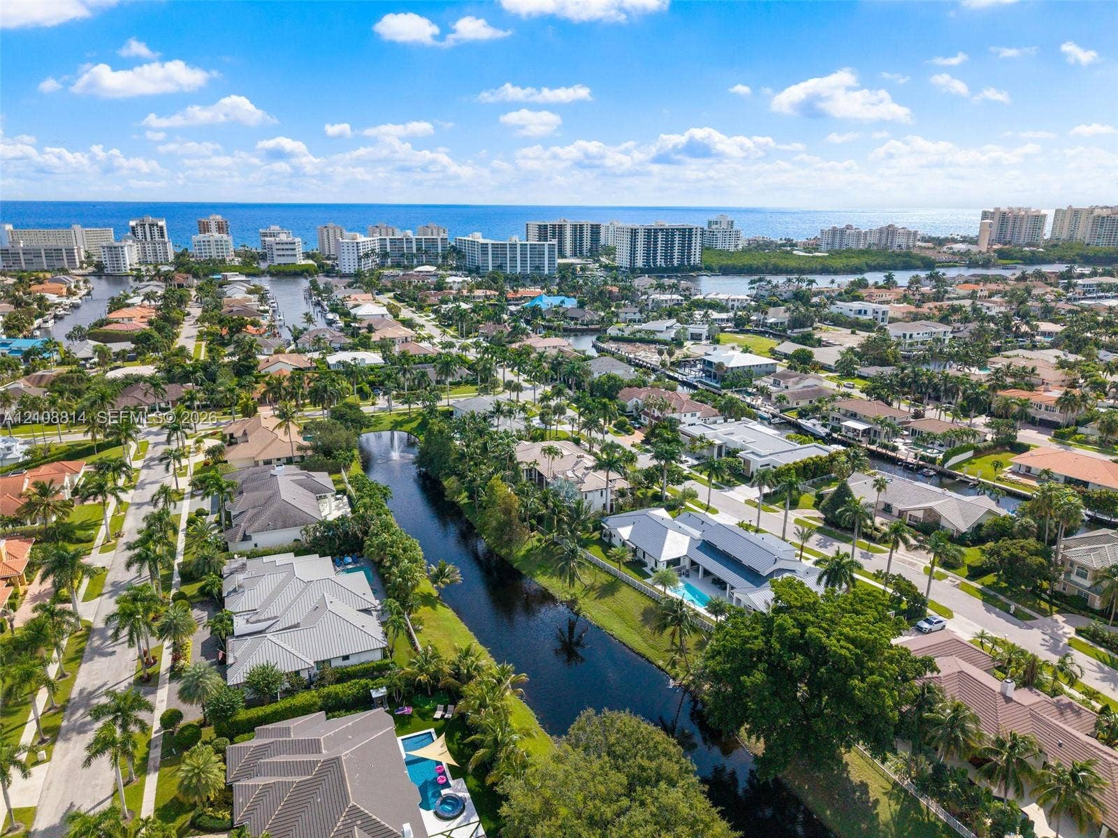 Aerial perspective of a coastal residential community featuring a network of canals, private swimming pools, mature palm trees, and residential architecture with multi-pitched rooflines