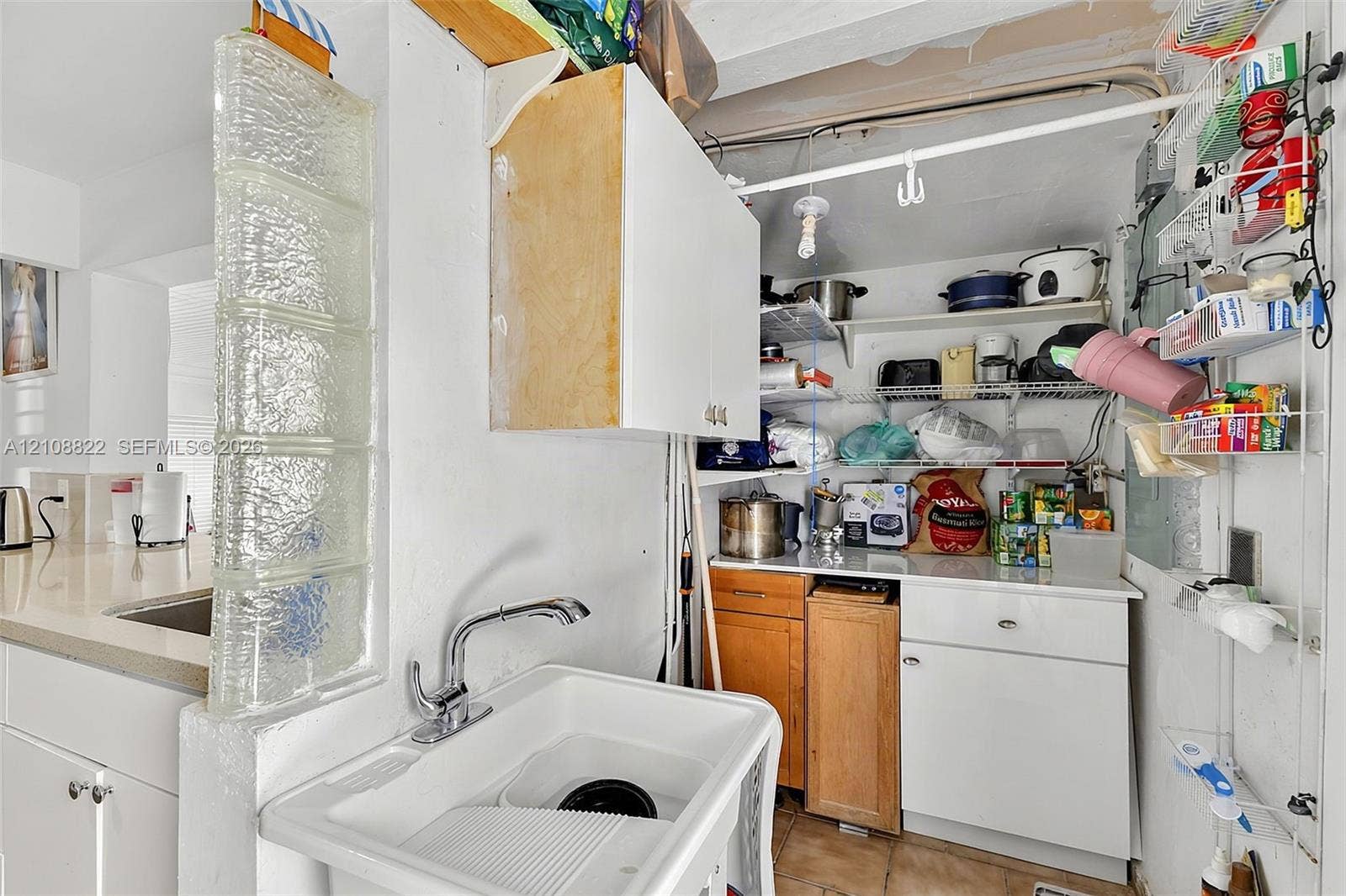 6838 SW 22nd Court, Miramar, FL 33023 Utility space featuring a glass block partition, a white deep-basin sink with a chrome faucet, built-in cabinetry, and open wire shelving