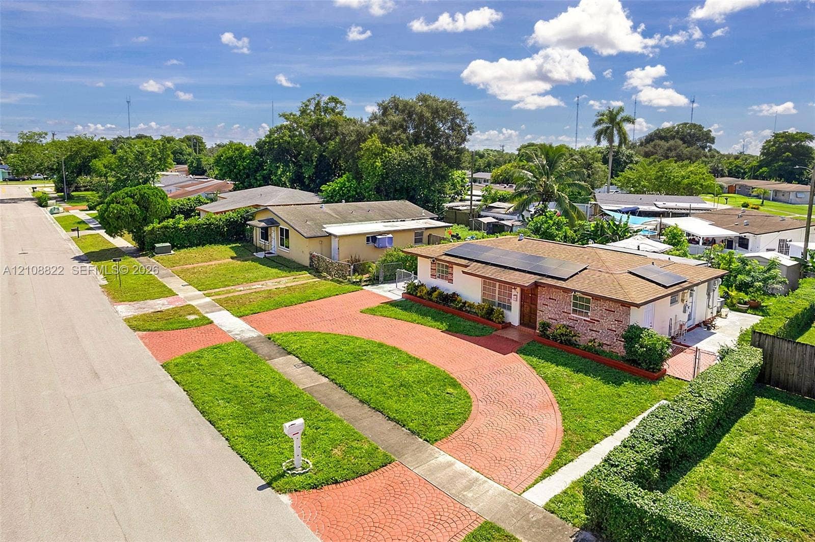 6838 SW 22nd Court, Miramar, FL 33023 Single-story residence featuring a brick and stucco exterior, roof-mounted solar panels, a circular paver driveway, and professional landscaping