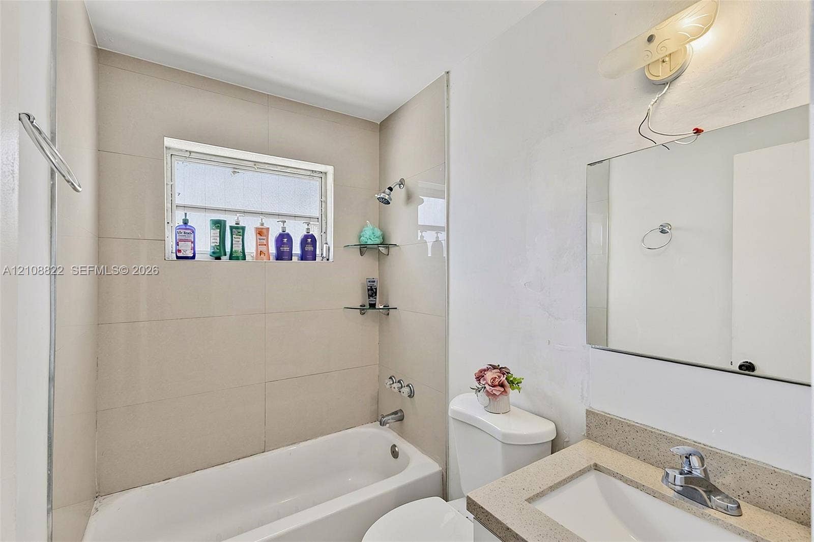 6838 SW 22nd Court, Miramar, FL 33023 Full bathroom featuring large-format wall tile, a built-in bathtub with showerhead, integrated glass corner shelving, a vanity with a solid surface countertop, and a wall-mounted light fixture