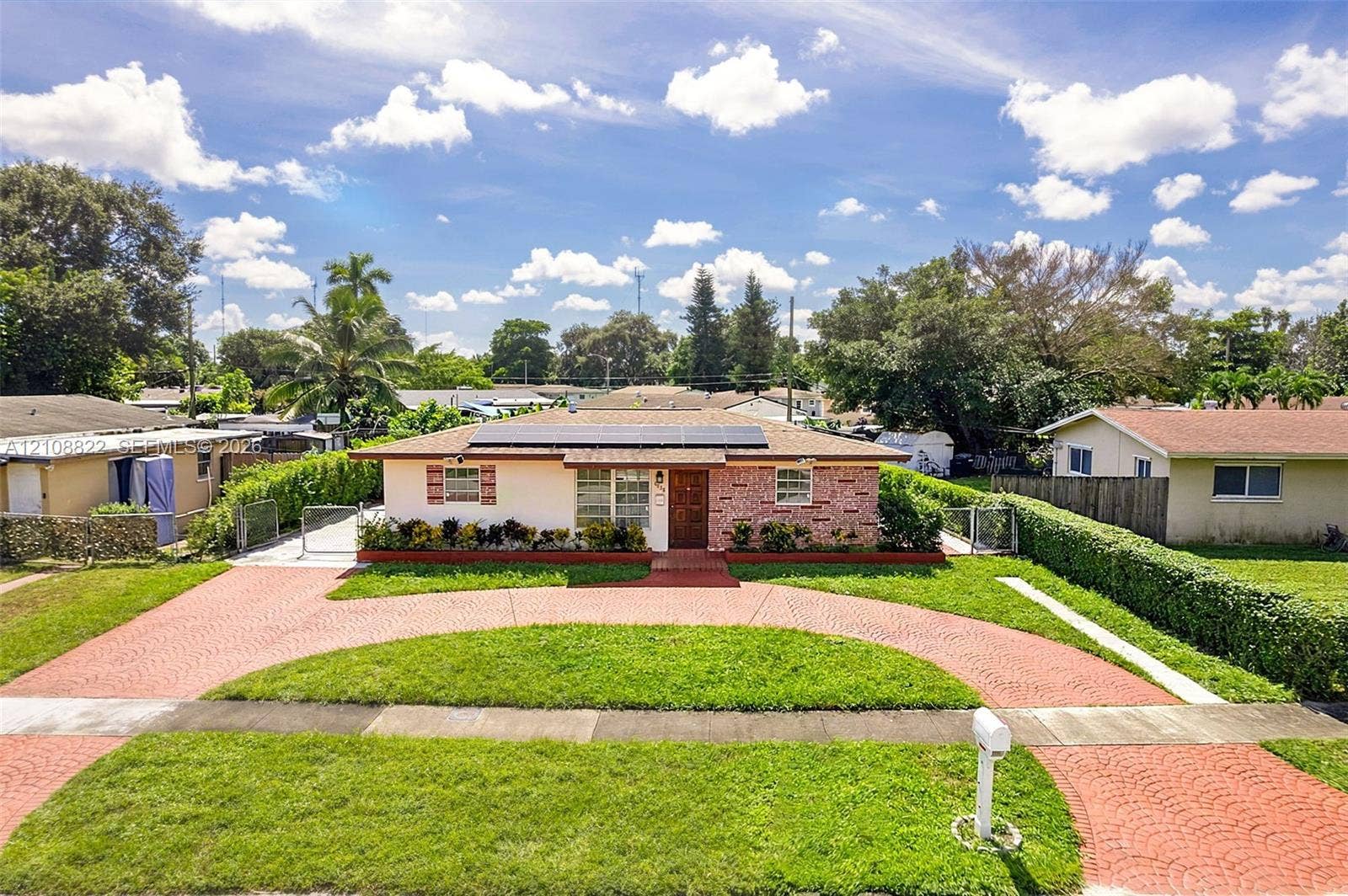 6838 SW 22nd Court, Miramar, FL 33023 Single-story exterior featuring a brick facade, rooftop solar panels, a semi-circular paved driveway, and manicured landscaping