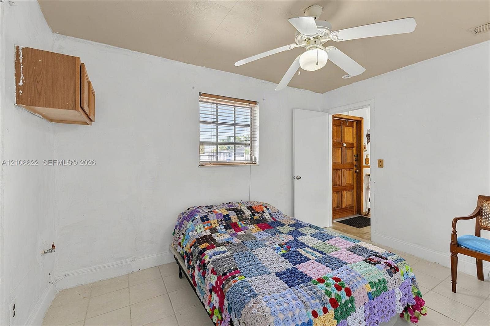 6838 SW 22nd Court, Miramar, FL 33023 Interior room featuring light-colored tile flooring, a centered ceiling fan with integrated lighting, a wall-mounted wooden cabinet, and a single-pane window with horizontal blinds