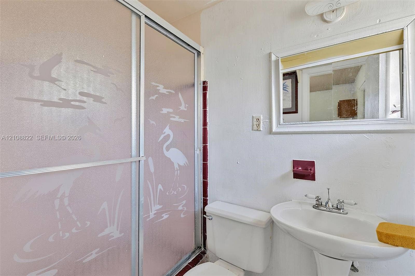 6838 SW 22nd Court, Miramar, FL 33023 Bathroom featuring a semi-frameless sliding glass shower enclosure with etched decorative detailing, a white pedestal sink with dual-handle chrome faucet, a rectangular wall-mounted mirror with integrated lighting, and a built-in recessed soap dish