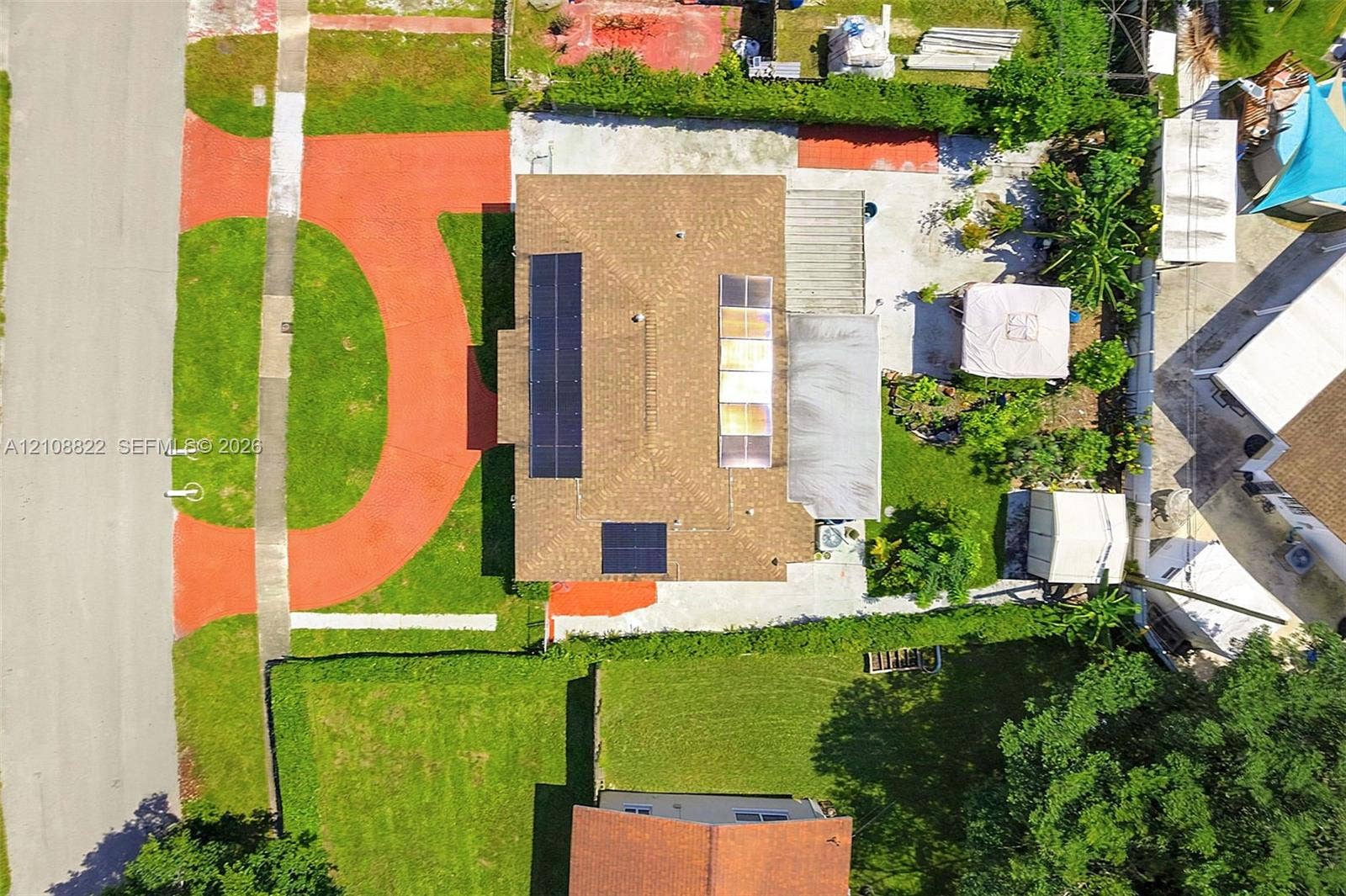 6838 SW 22nd Court, Miramar, FL 33023 Aerial perspective featuring a residential lot with solar panel arrays, a multi-section roof, a paved concrete driveway, and mature landscaping