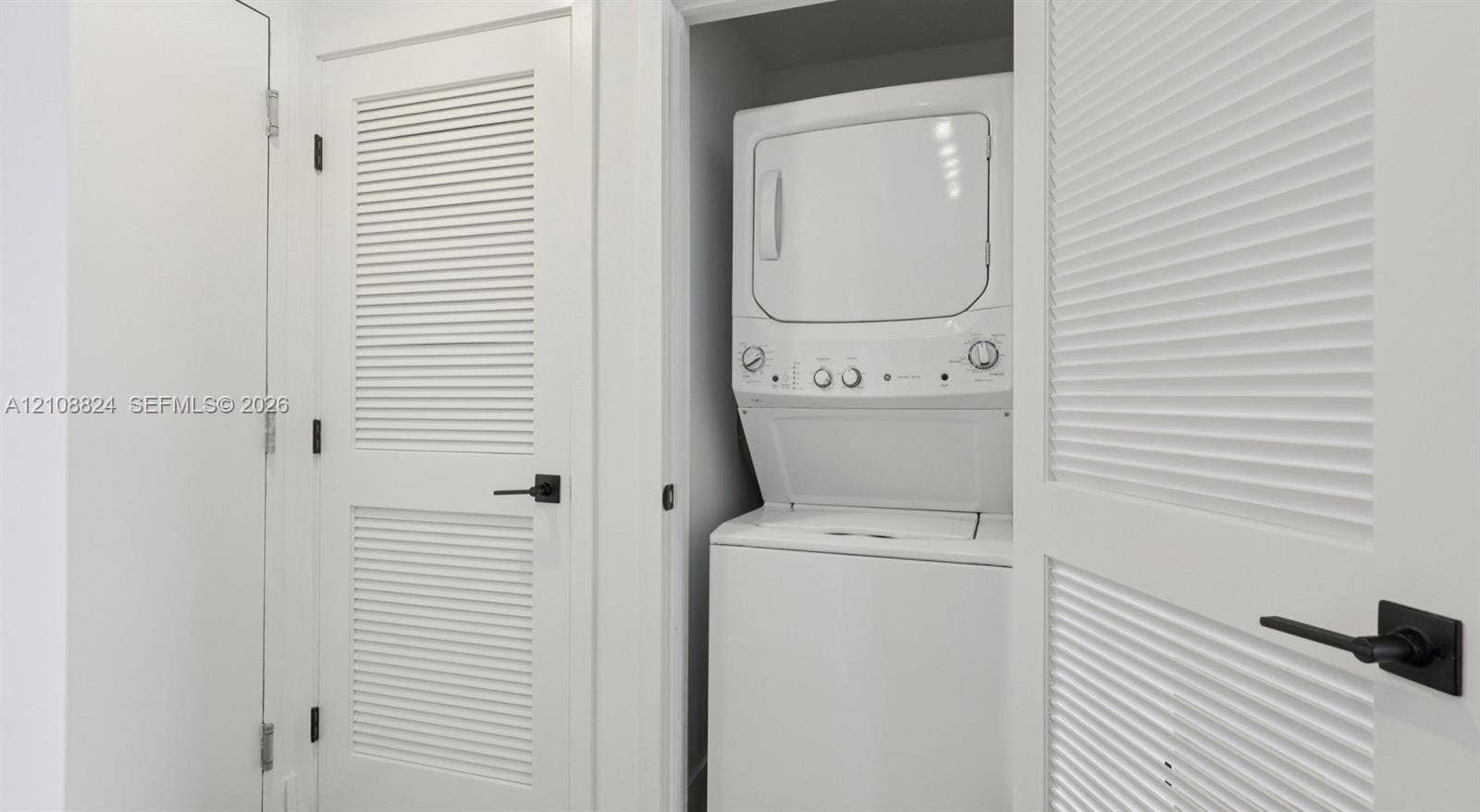 Laundry closet featuring a stackable washer and dryer unit, white louvered doors, and matte black hardware