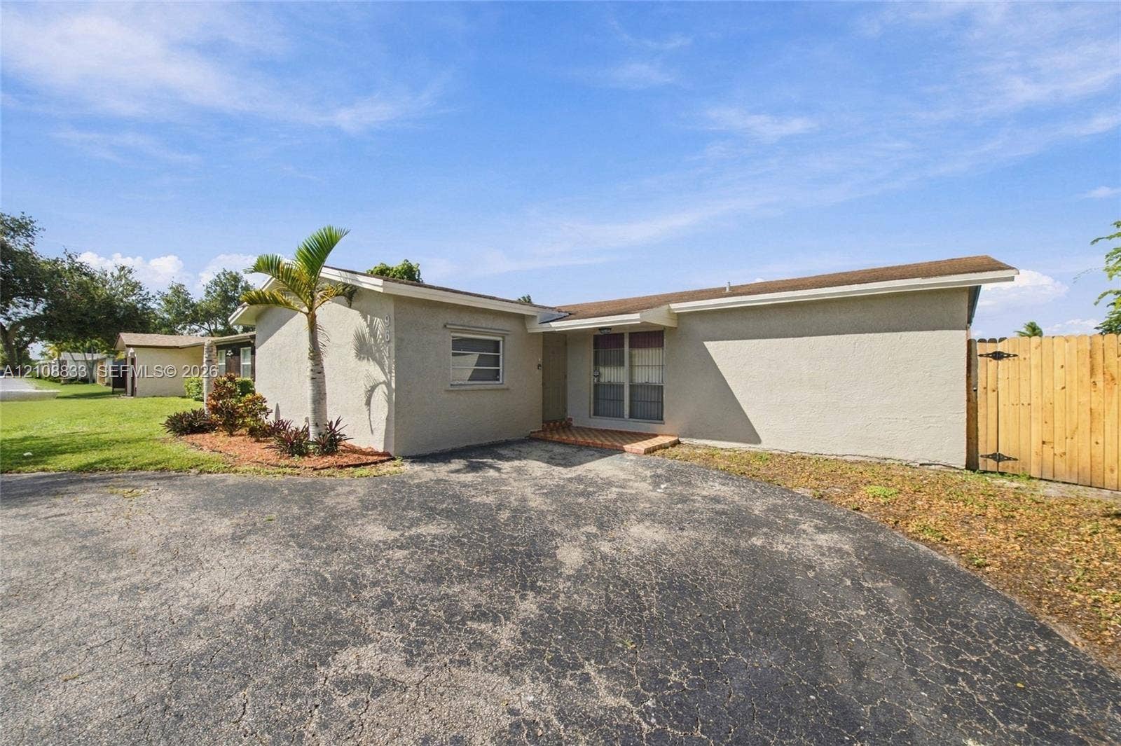 9611 Johnson Street, Pembroke Pines, FL 33024 Single-story exterior featuring a light-toned stucco facade, expansive asphalt driveway, and tall wood privacy fencing