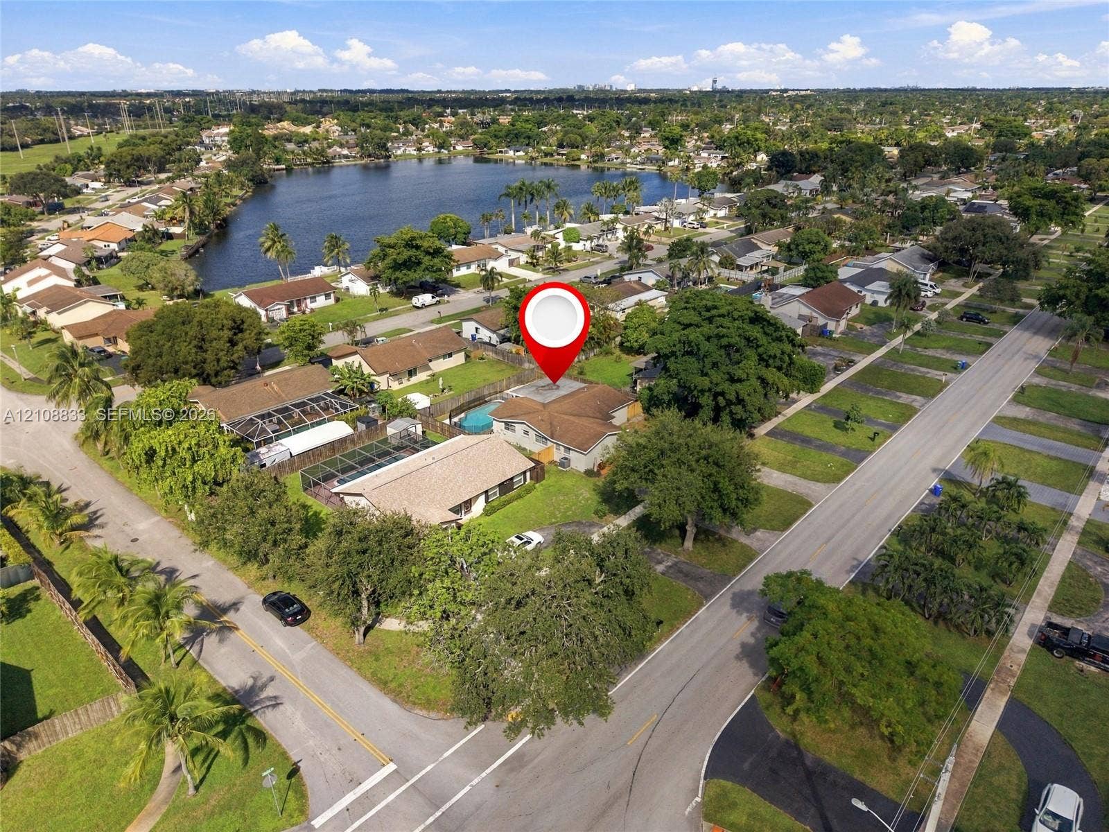 9611 Johnson Street, Pembroke Pines, FL 33024 Aerial perspective of a single-story residence featuring a shingled roof, an in-ground swimming pool with a screen enclosure, and mature landscaping