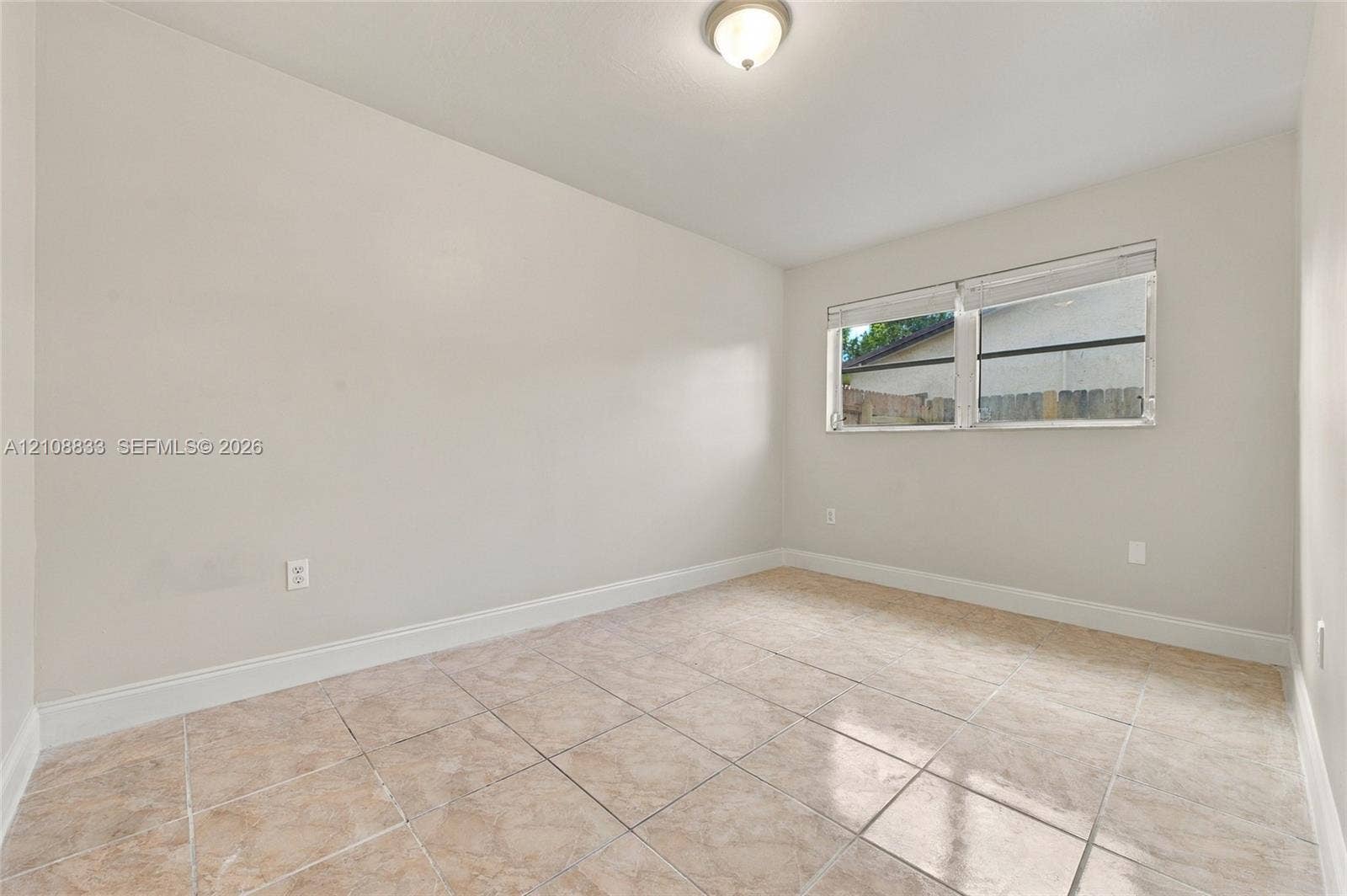 9611 Johnson Street, Pembroke Pines, FL 33024 Neutral-toned interior space featuring large-format tile flooring, a dual-pane horizontal sliding window, and a ceiling-mounted flush light fixture