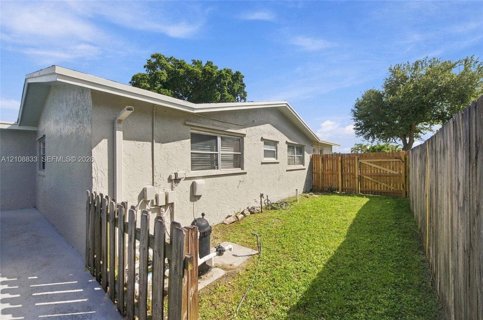 9611 Johnson Street, Pembroke Pines, FL 33024 Exterior side yard featuring stucco siding, horizontal sliding windows, a manicured lawn, and wood privacy fencing with an integrated gate