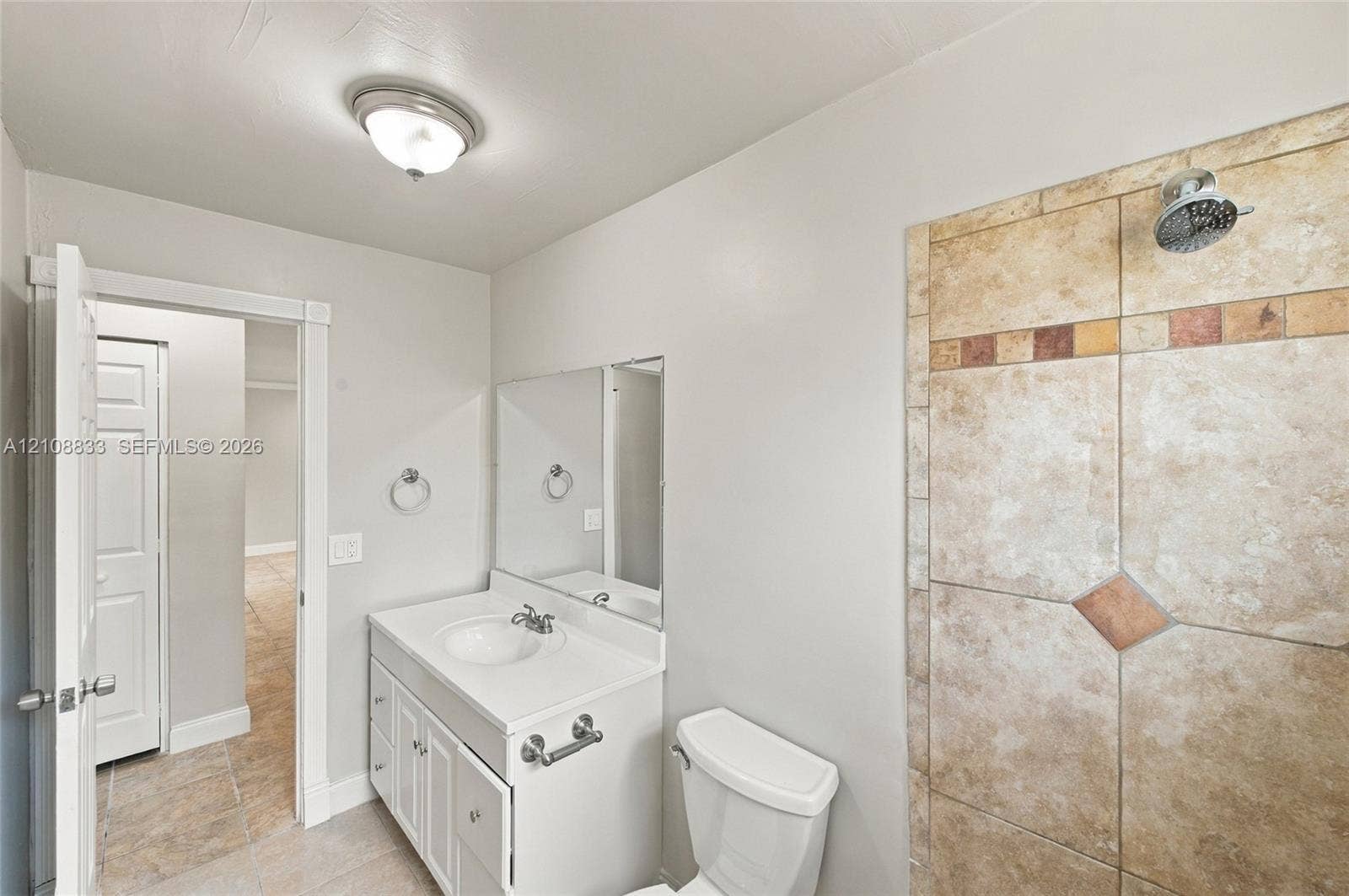 9611 Johnson Street, Pembroke Pines, FL 33024 Bathroom featuring white cabinetry, integrated sink, wall-mounted mirror, and tile-surround shower with decorative stone-finish accents