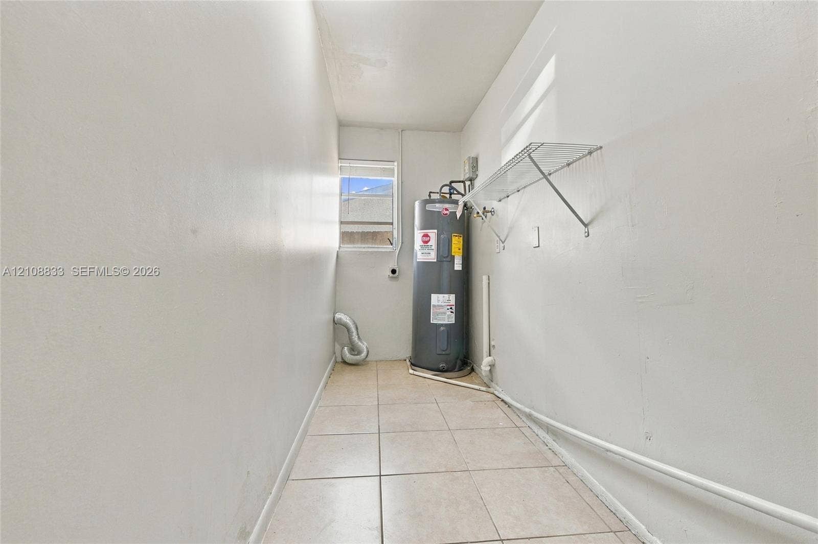 9611 Johnson Street, Pembroke Pines, FL 33024 Utility space featuring light-toned tile flooring, a window, wall-mounted wire shelving, and an installed water heater