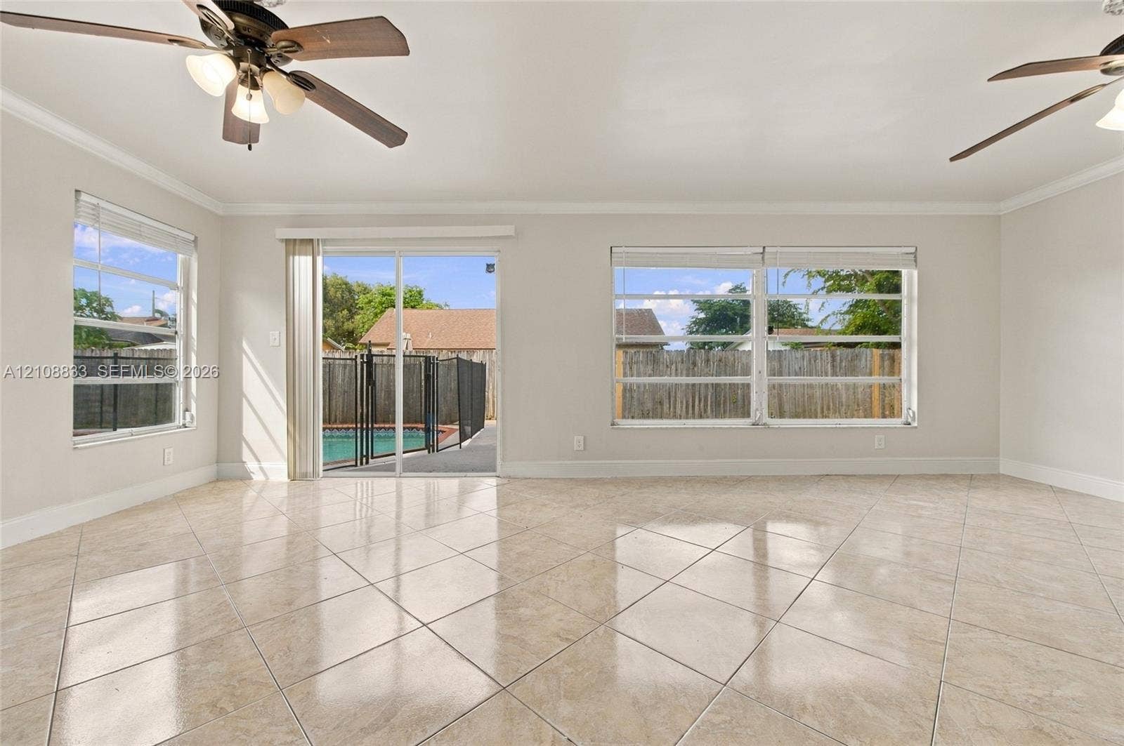 9611 Johnson Street, Pembroke Pines, FL 33024 Neutral-toned interior featuring large-format tile flooring, dual ceiling fans with integrated light fixtures, and expansive windows