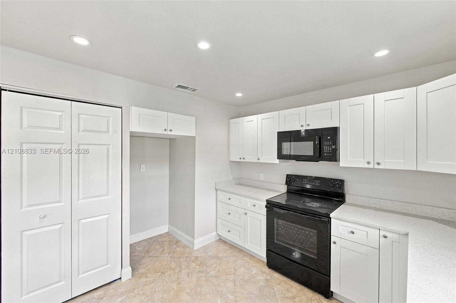 9611 Johnson Street, Pembroke Pines, FL 33024 Kitchen featuring white shaker-style cabinetry, solid-surface countertops, black range with matching over-the-range microwave, and tile flooring