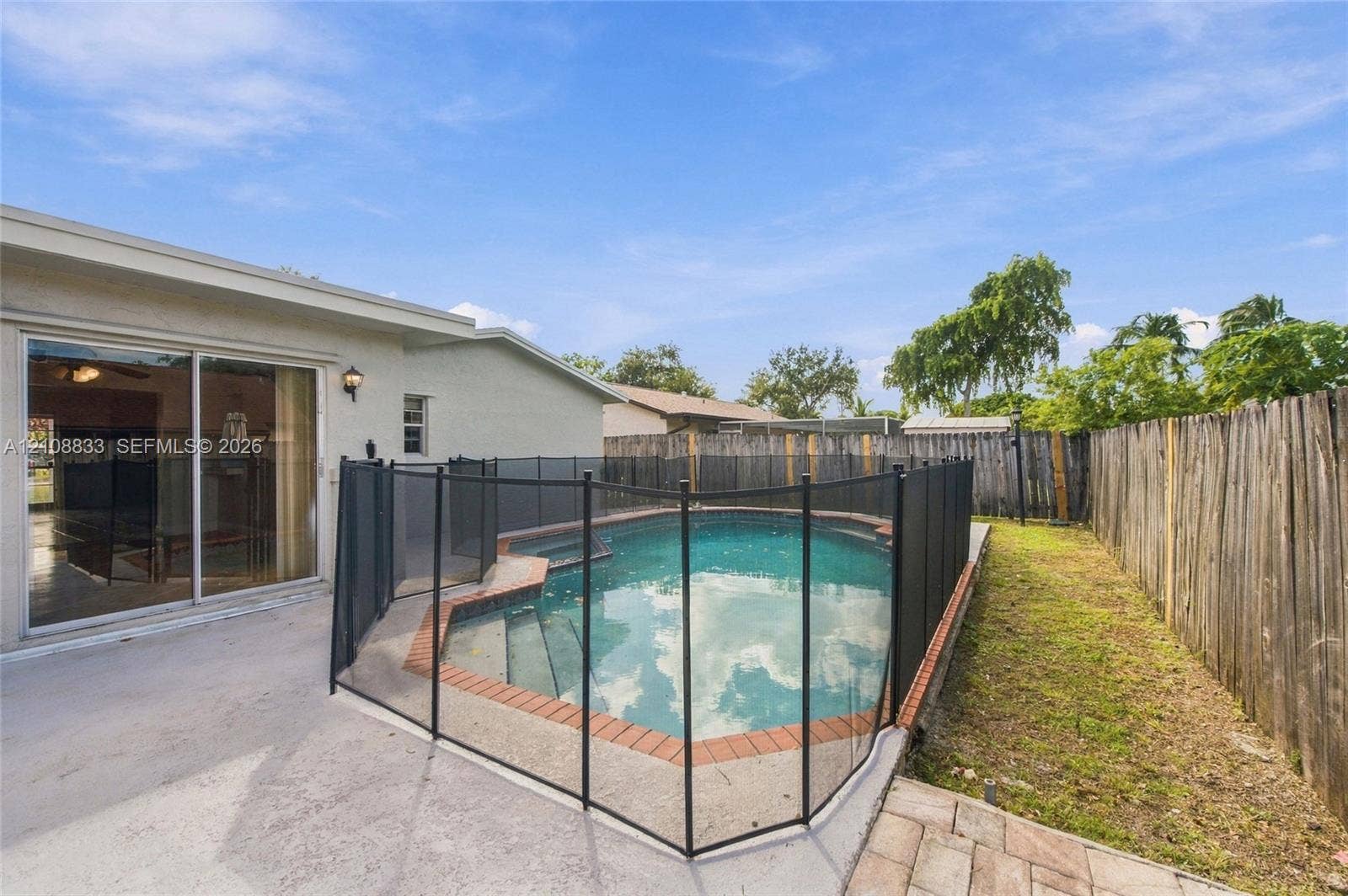 9611 Johnson Street, Pembroke Pines, FL 33024 Backyard featuring an in-ground swimming pool with brick coping, a protective mesh safety fence, a concrete patio, and a wood privacy fence