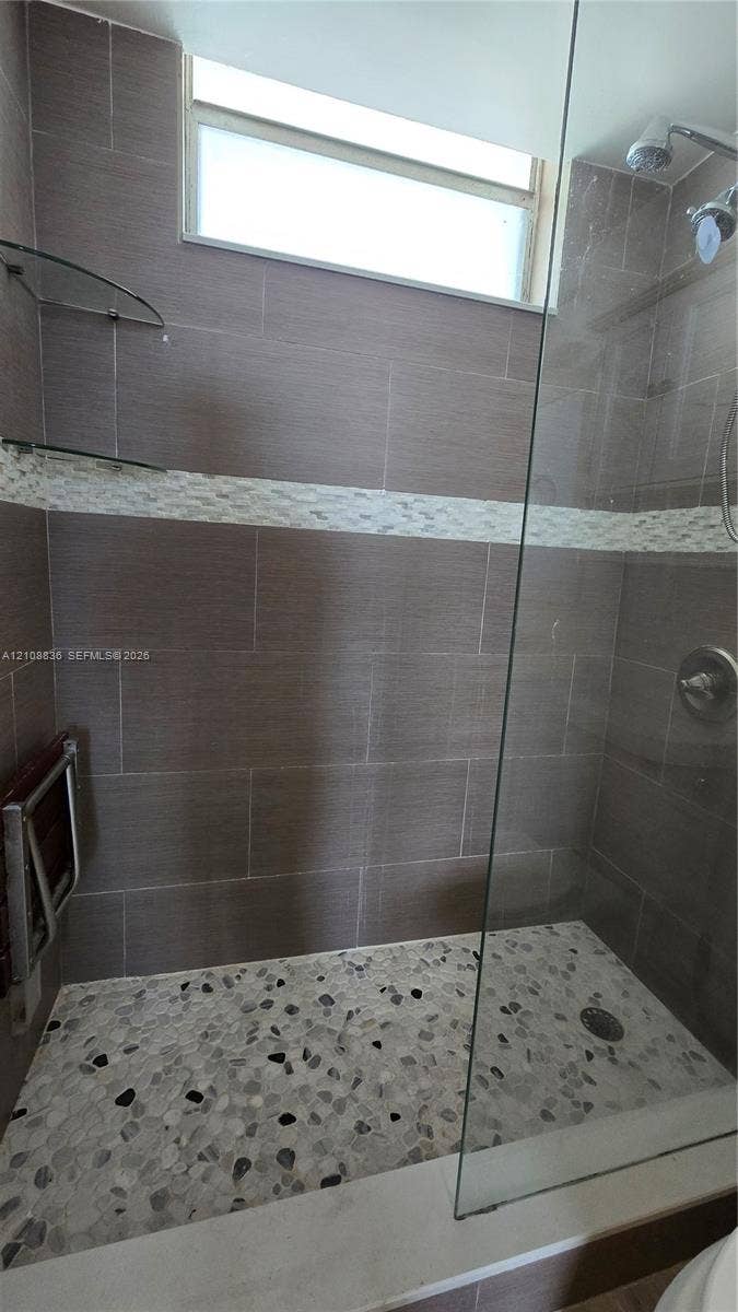 3000 Marcos Drive, #P304, Aventura, FL 33160 Walk-in shower featuring large-format wall tile, a horizontal decorative mosaic tile accent, pebble-style floor tiling, a glass enclosure, and a transom window