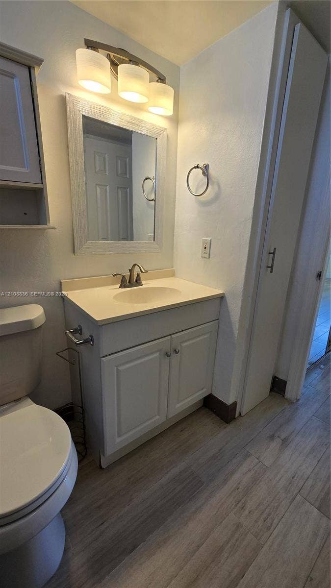 3000 Marcos Drive, #P304, Aventura, FL 33160 Bathroom featuring a vanity with shaker-style cabinetry, solid surface countertop, wood-finish flooring, and a three-light wall-mounted fixture