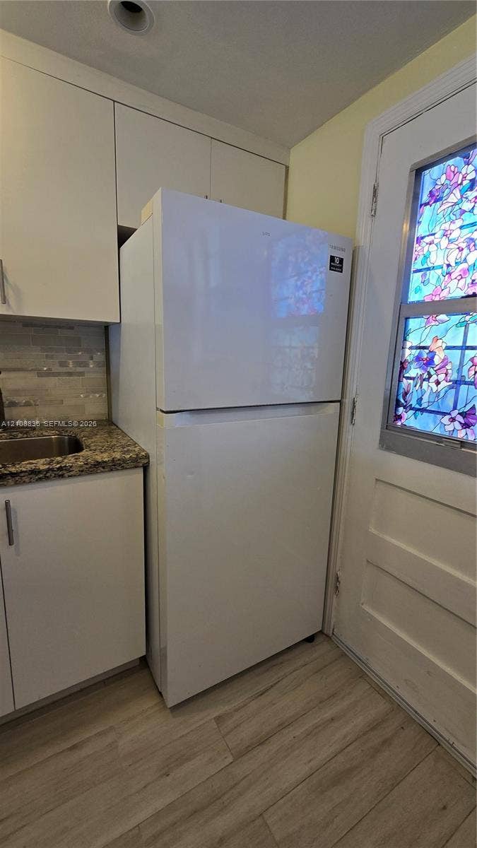 3000 Marcos Drive, #P304, Aventura, FL 33160 Kitchen area featuring white cabinetry, stone-finish countertops, wood-finish flooring, and a door with a decorative stained-glass insert