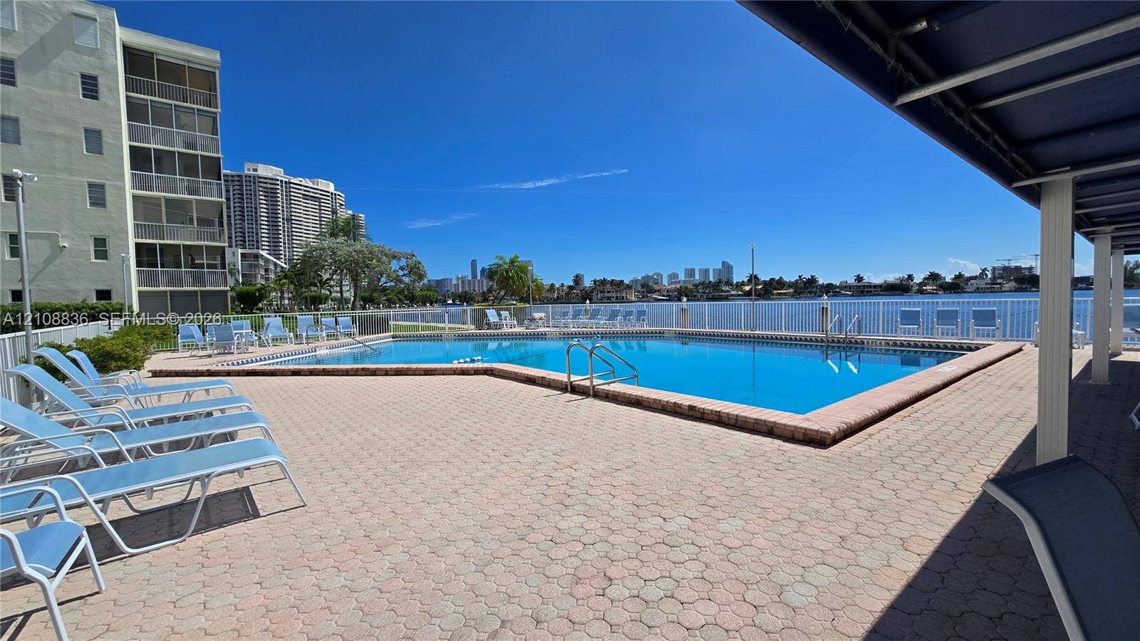 3000 Marcos Drive, #P304, Aventura, FL 33160 Waterfront swimming pool featuring paver decking, white metal safety fencing, and an overhead canopy structure