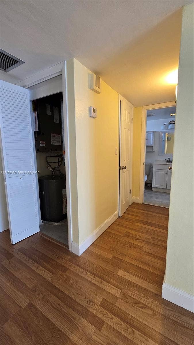 3000 Marcos Drive, #P304, Aventura, FL 33160 Hallway featuring wood-finish flooring, louvered closet doors, and a utility closet containing a water heater and HVAC unit