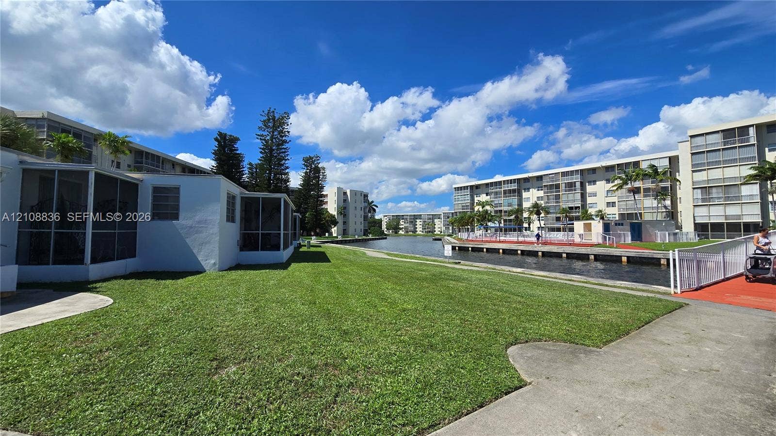 3000 Marcos Drive, #P304, Aventura, FL 33160 Ground-level exterior featuring screen-enclosed patios, expansive turf lawn, concrete walkways, and canal frontage