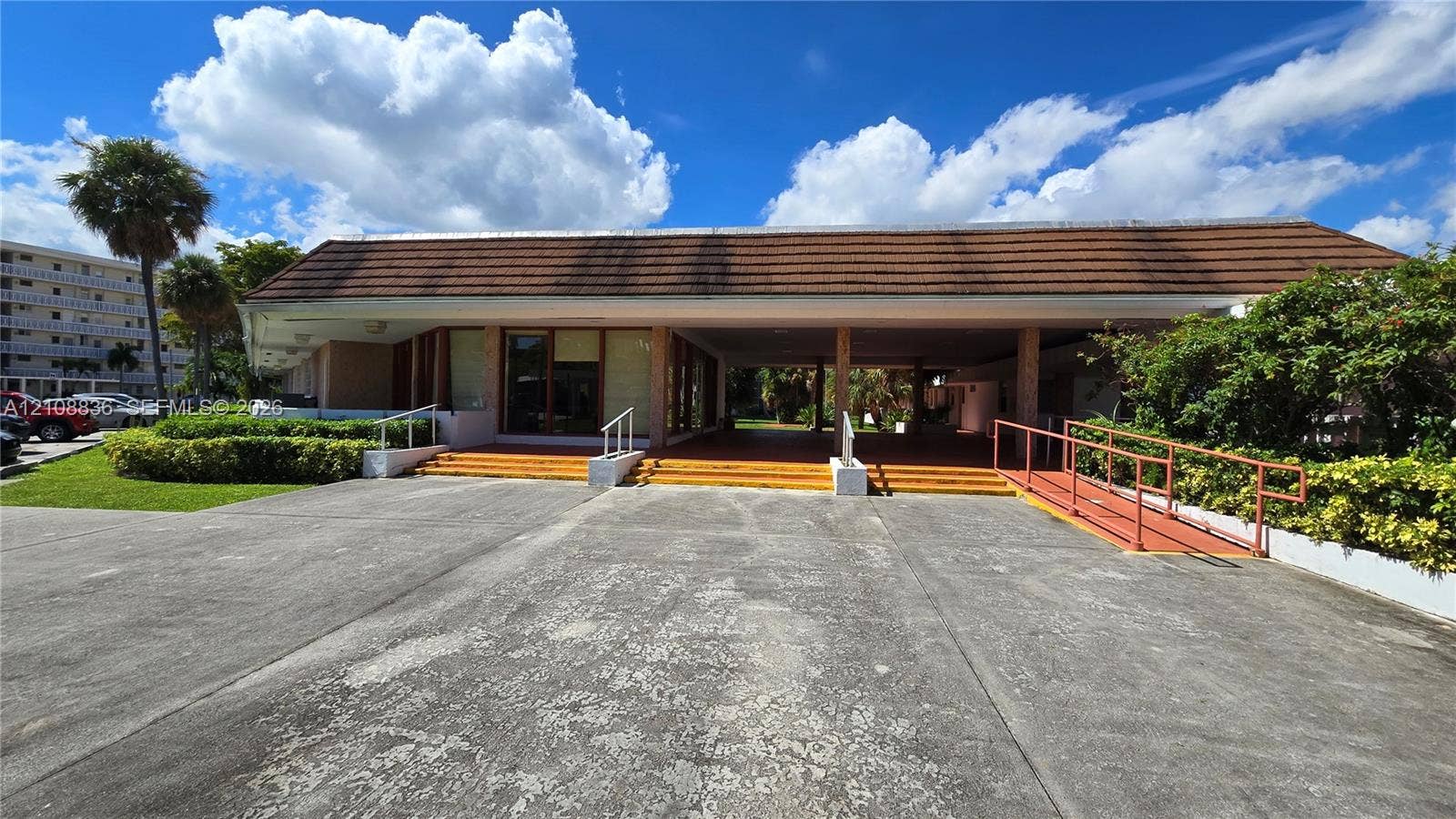 3000 Marcos Drive, #P304, Aventura, FL 33160 Exterior facade featuring a wide covered entryway, terra-cotta style tiled steps, structural support columns, and an integrated metal access ramp