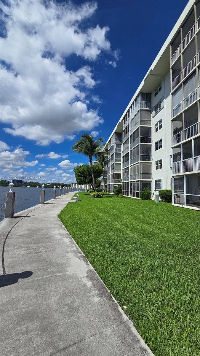 3000 Marcos Drive, #P304, Aventura, FL 33160 Concrete waterfront promenade featuring a metal-post rope railing, expansive manicured lawn, and multi-story building exterior with stacked screened balconies
