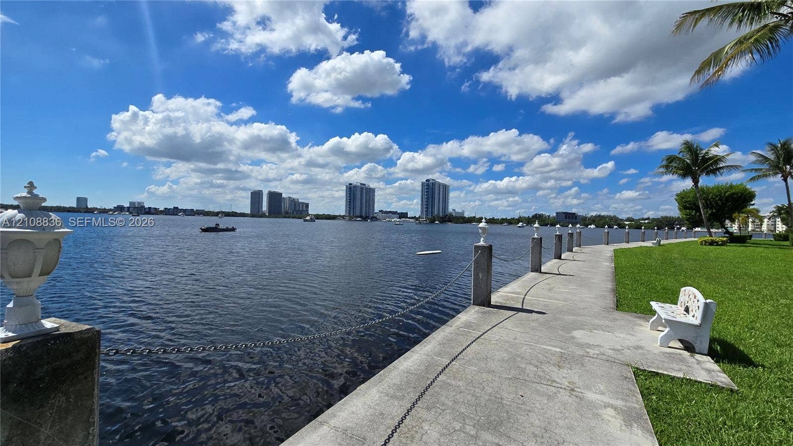 3000 Marcos Drive, #P304, Aventura, FL 33160 Waterfront concrete walkway featuring a post-and-chain barrier, decorative pedestal lighting, and manicured lawn