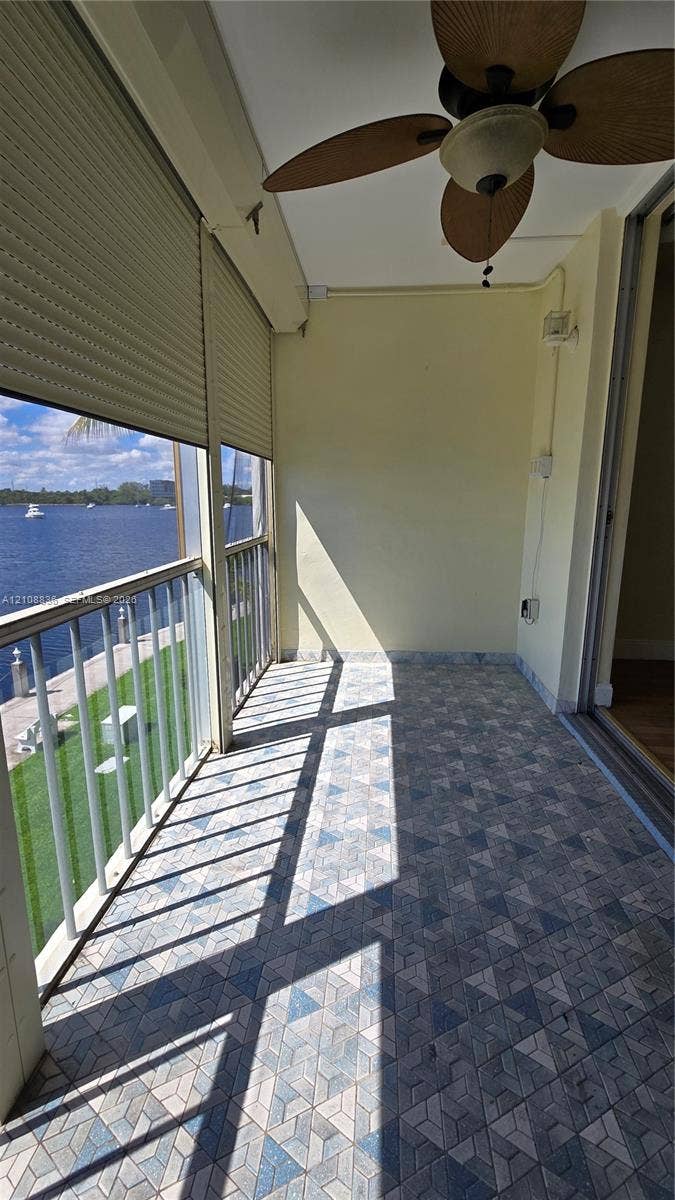 3000 Marcos Drive, #P304, Aventura, FL 33160 Covered balcony featuring patterned tile flooring, a ceiling-mounted paddle fan, integrated roll-down security shutters, and metal railing overlooking the waterway