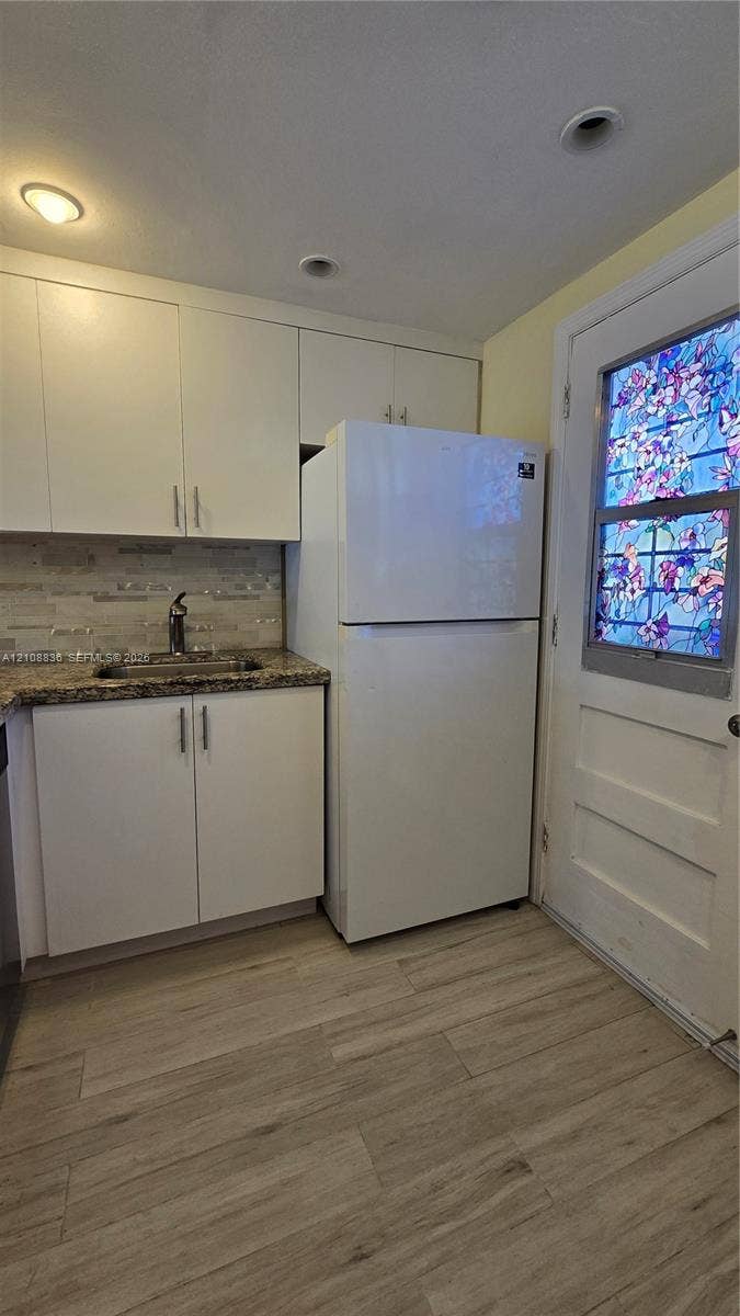 3000 Marcos Drive, #P304, Aventura, FL 33160 Kitchenette featuring white shaker-style cabinetry, stone-surface countertops, textured tile backsplash, wood-finish flooring, and a decorative stained-glass panel door