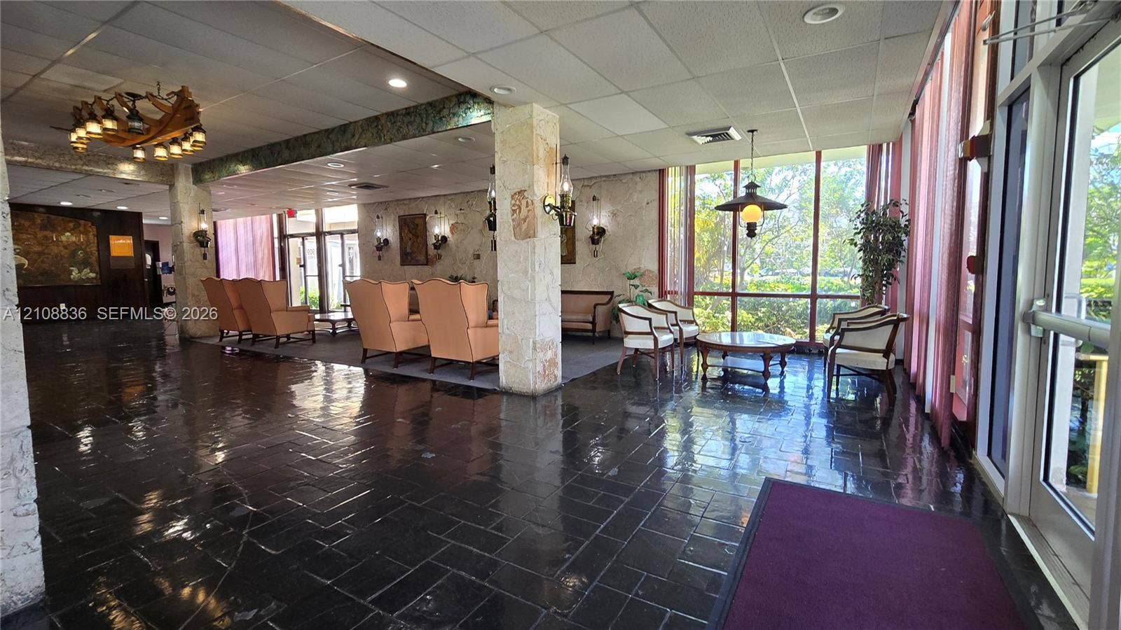 3000 Marcos Drive, #P304, Aventura, FL 33160 Spacious lobby featuring stone-clad structural pillars, dark stone tile flooring, floor-to-ceiling windows, and decorative chandelier lighting