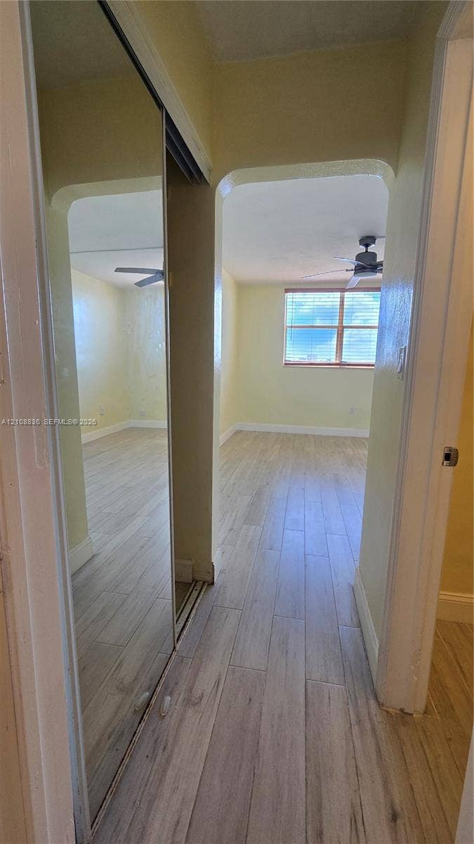 3000 Marcos Drive, #P304, Aventura, FL 33160 Full-height mirrored sliding closet doors featuring wood-finish flooring, arched doorway detail, and a ceiling-mounted fan fixture