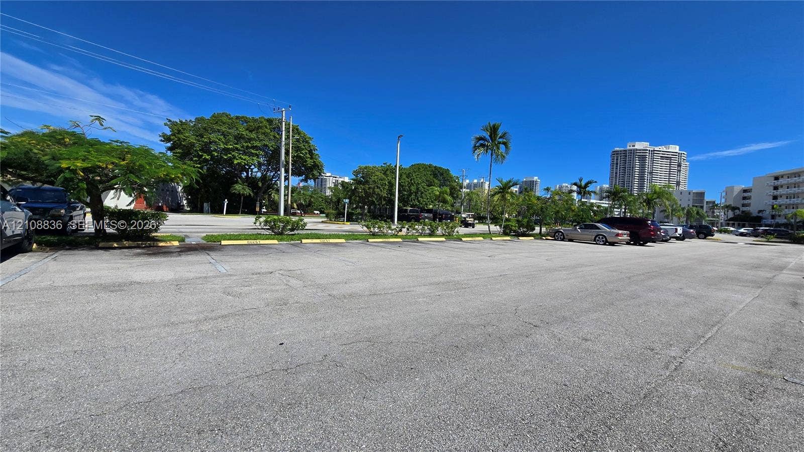 3000 Marcos Drive, #P304, Aventura, FL 33160 Asphalt-paved parking lot featuring designated parking stalls, yellow concrete wheel stops, and mature landscaping