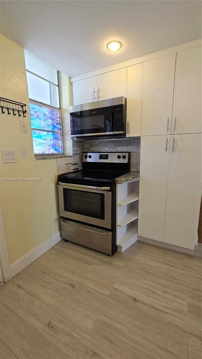 3000 Marcos Drive, #P304, Aventura, FL 33160 Kitchen featuring white cabinetry with brushed-nickel hardware, stainless steel appliances, stone-look countertops, tile backsplash, and light wood-finish flooring