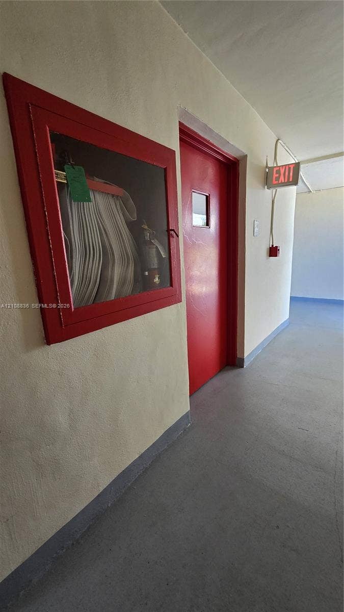3000 Marcos Drive, #P304, Aventura, FL 33160 Hallway featuring a painted metal door, wall-mounted fire safety cabinet with glass panel, and illuminated exit signage