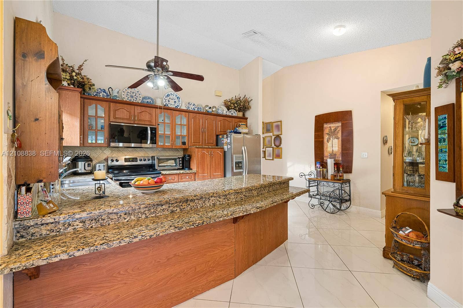 Kitchen featuring stone-surfaced breakfast bar, wood cabinetry, built-in stainless steel microwave, and tile flooring
