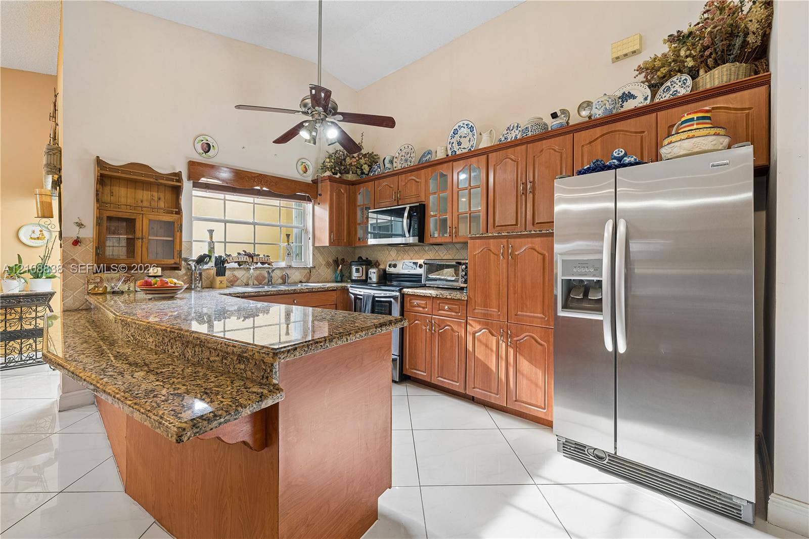 Kitchen featuring wood cabinetry, stone countertops with an integrated breakfast bar, stainless steel side-by-side refrigerator, tile flooring, and vaulted ceilings